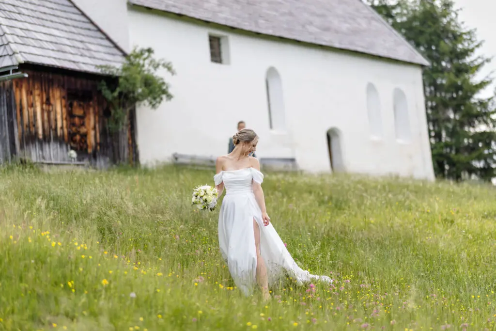 Braut im weißen Kleid auf der Almwiese Braut im weißen Hochzeitskleid auf einer Almwiese vor einer Kirche auf der Turracher Höhe